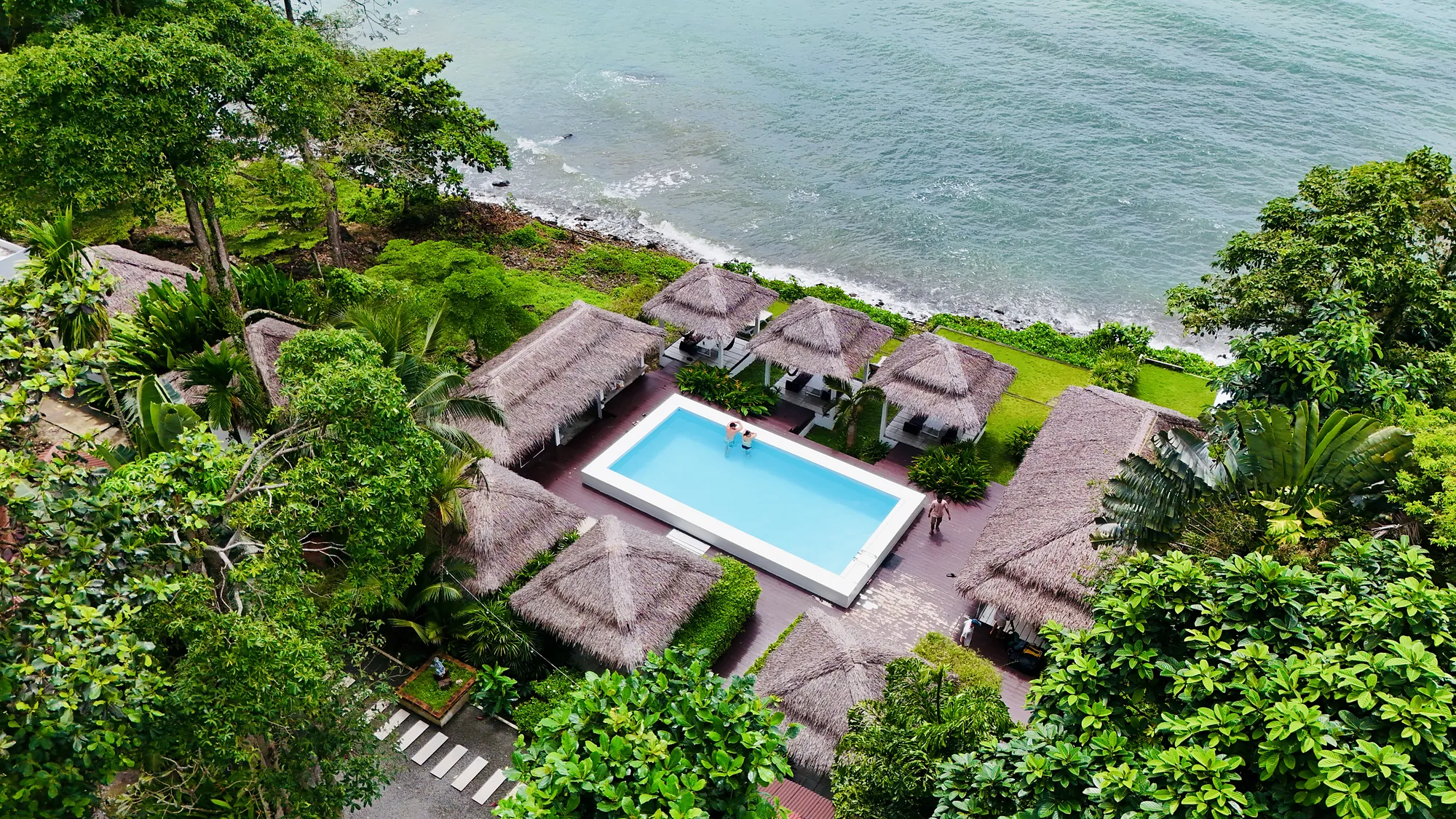 Aerial view of the resort on the coast: the pool, the thatched salas and the sea