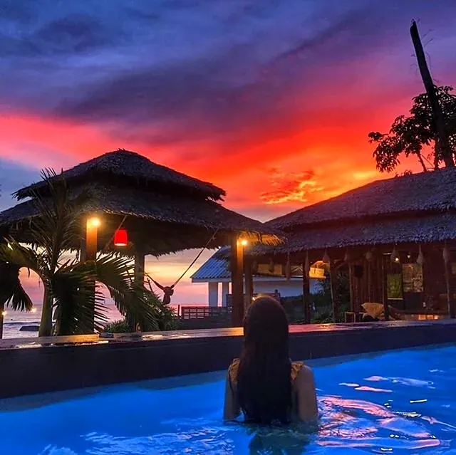 Swimmer in the pool at dusk with a red sky