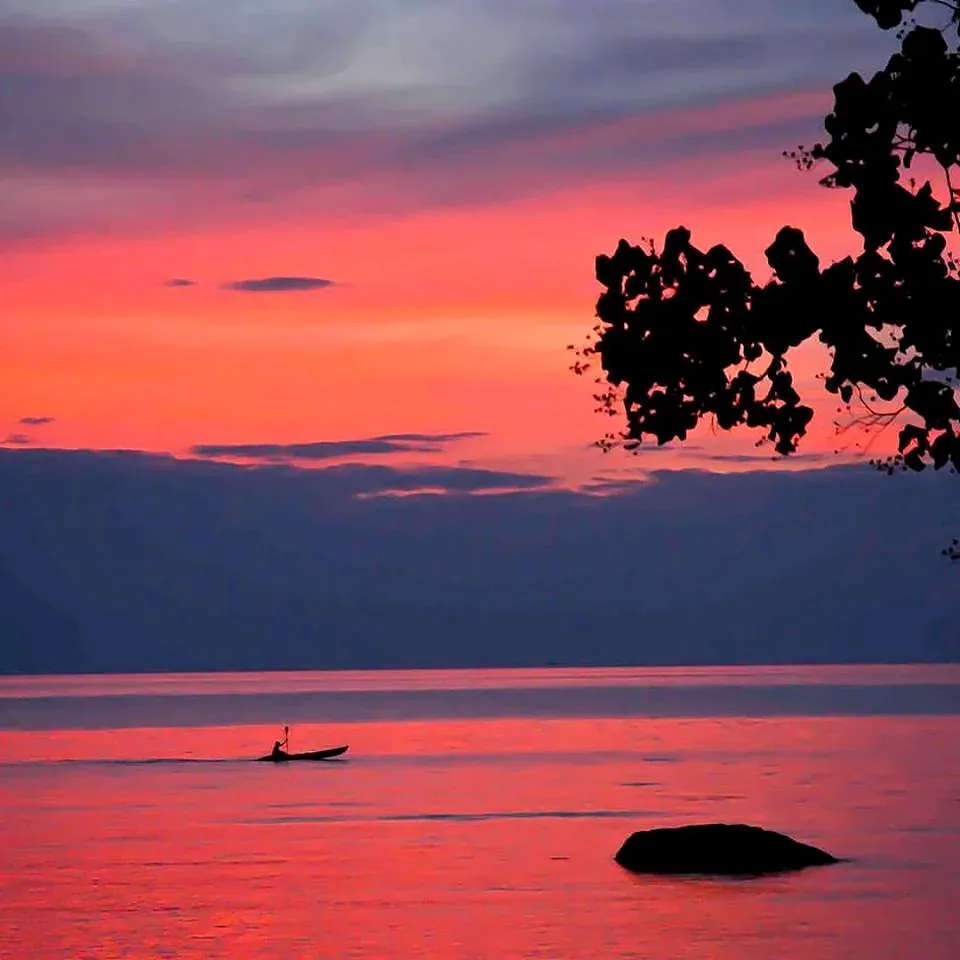 A longtail boat on a red sea at sunset off Lonely Beach