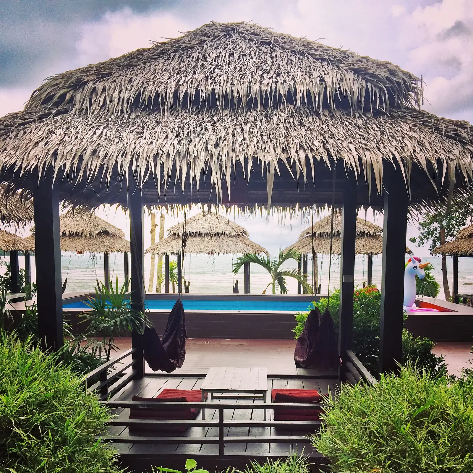 Thatched sala with hammocks and cushions looking over the pool to the sea